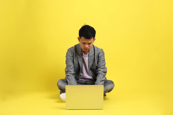The Asian LGBTQ man with grey blazer sitting on the yellow background. - 写真・画像