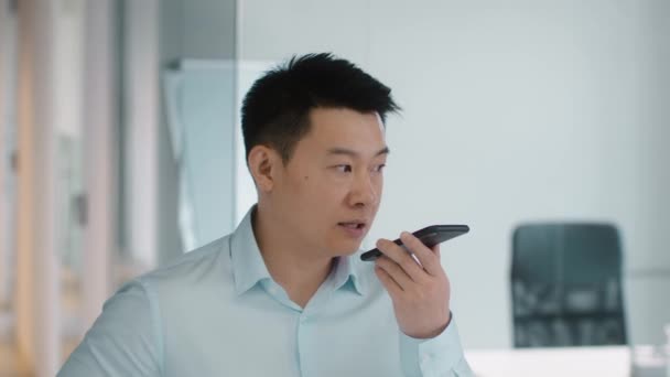 Fast modern communication. Close up portrait of serious mature asian businessman recording voice message on smartphone, standing at office, slow motion - Felvétel, videó