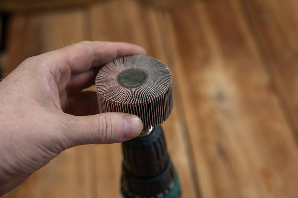 Man places flap wheel in cam of an electric drill chuck. Tool for woodworking, sanding, removing rust from various surfaces. Yellow wooden boards defocused in background. Close-up. Selective focus. - Fotografie, Obrázek