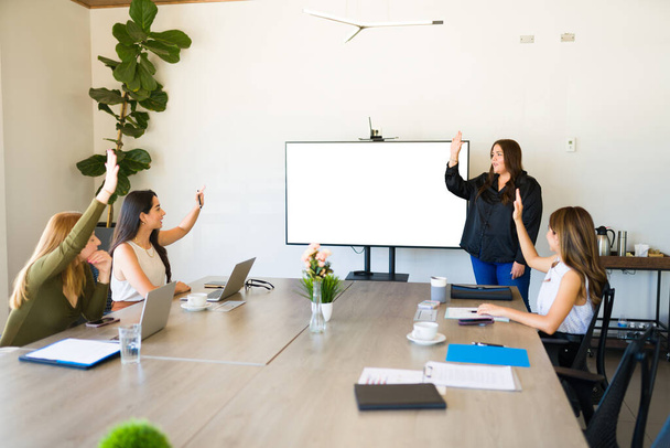Профессиональные женщины и деловые партнеры поднимают руки и голосуют во время встречи с командой в офисе - Фото, изображение