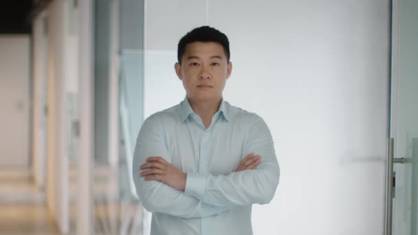 Professionalism concept. Indoors portrait of confident middle aged asian businessman posing with folded arms at office interior, looking at camera, slow motion - Video