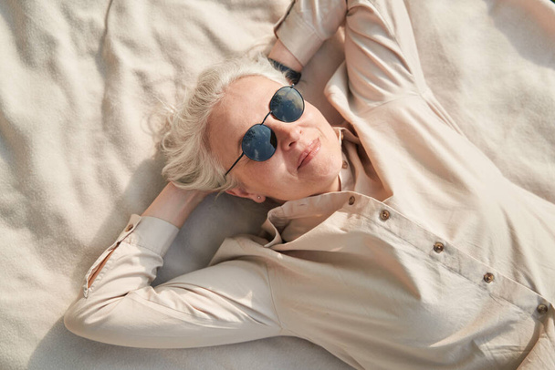 Счастливая зрелая женщина лежит на одеяле, наслаждаясь видом на природу - Фото, изображение