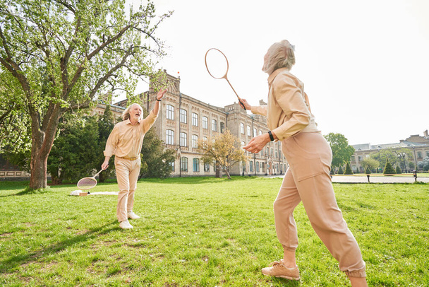 Aged man raising his arm while playing badminton with his wife - Photo, image