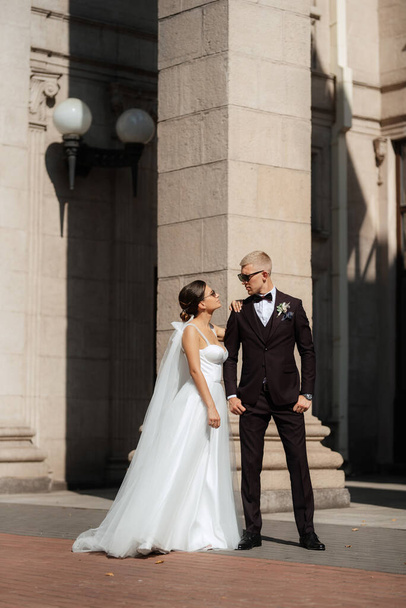 the groom in a brown suit and the bride in a white dress in an urban atmosphere - Фото, изображение