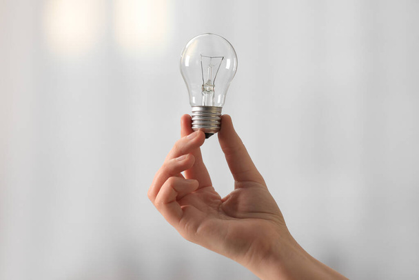 Woman holding light bulb on blurred background, closeup - Фото, изображение