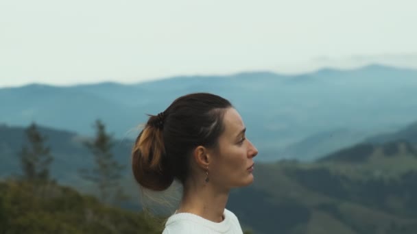 Face young woman, side view, stands mountains looks into distance. Clouds, green hills, beautiful view. Concept, peace, tranquility, contemplation, nature, travel, tourism, hiking. High quality 4k - Záběry, video