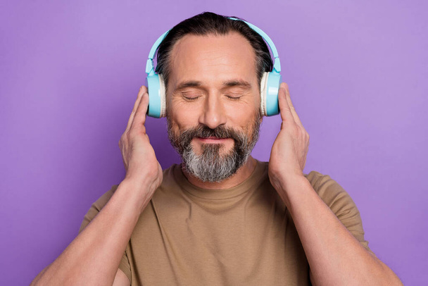 Portrait of handsome middle age man meditating while listening classical peaceful music isolated on violet color background. - Фото, изображение