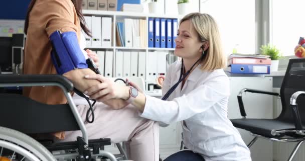 Az orvos ellenőrzi a kerekesszékes terhes nő vérnyomását. Fogyatékkal élő terhes nők nőgyógyásza és orvosi ellenőrzése - Felvétel, videó