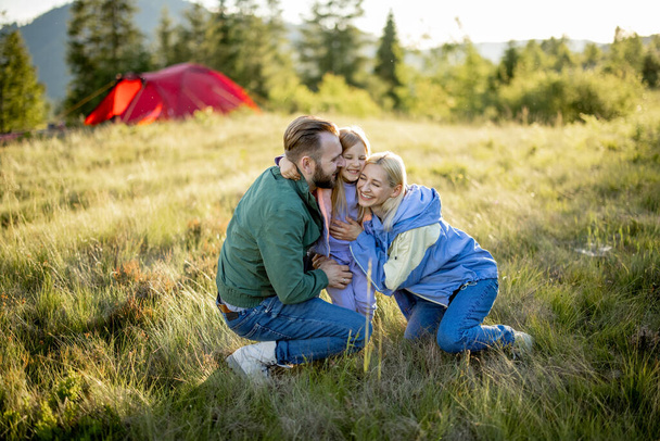 Portrét krásného páru s holčičím objetím při cestování v horách. Mladá bělošská rodina tráví letní čas na přírodě - Fotografie, Obrázek