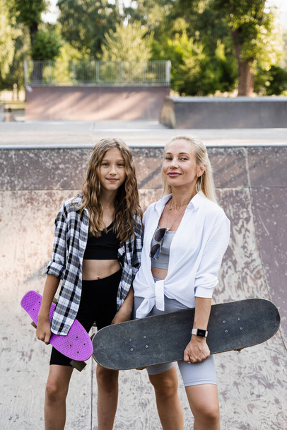 Mother and child daughter with skate and penny board training together in skate park. Extreme lifestyle. Family of mom and her kid spend time together - Valokuva, kuva