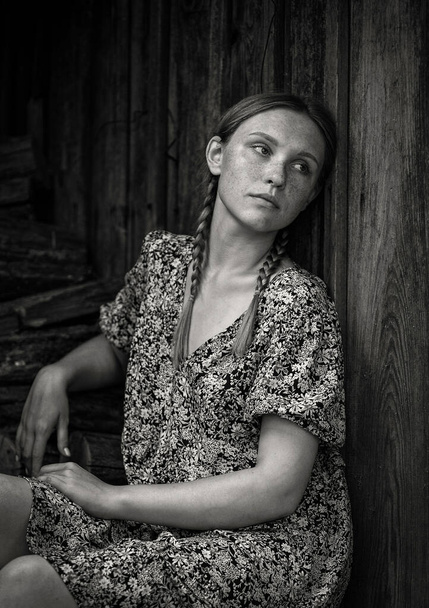 Een jong meisje zit buiten het dorpshuis op een hete zomerdag met haar hoofd gebogen. - Foto, afbeelding