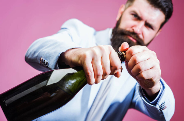 Un uomo barbuto che cerca di aprire una bottiglia di vino con le mani. Brutale bel maschio con champagne - Foto, immagini