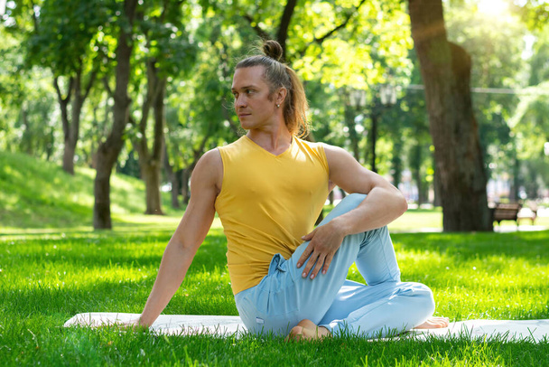 Un joven practica yoga en el parque. Asanas de yoga en parque de la ciudad, día soleado. Concepto de meditación, bienestar y estilo de vida saludable - Foto, imagen