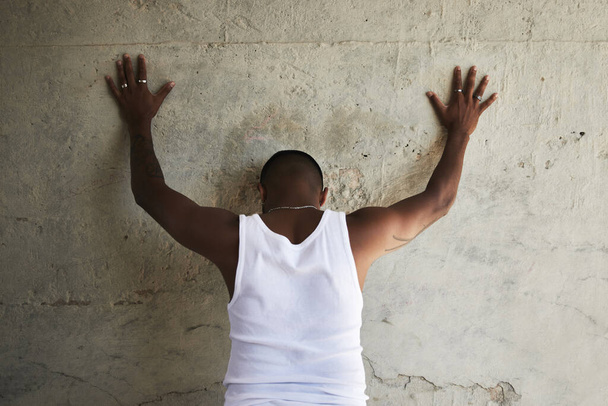 Achteraanzicht foto van een man leunend tegen een stadsmuur met zijn handen omhoog. - Foto, afbeelding