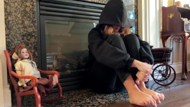 offended teenager teenager girl sitting by the fireplace with her legs bent and her head bowed she pulled the hood over her face she has a black sweatshirt and black jeans sadness of adolescence - Footage, Video