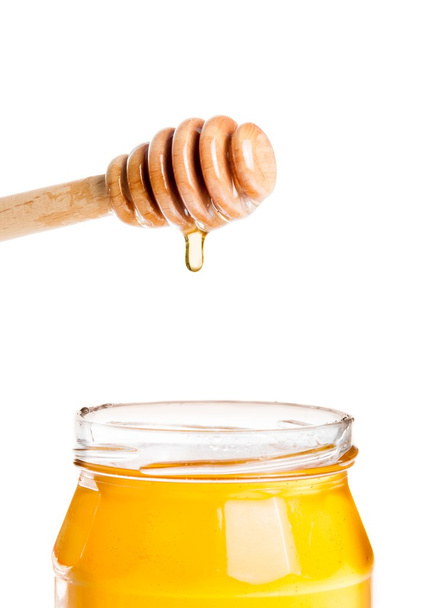 geöffnetes Honigglas auf weißem Hintergrund mit hölzernem Honiglöffel oben mit Tropfenhonig - Foto, Bild