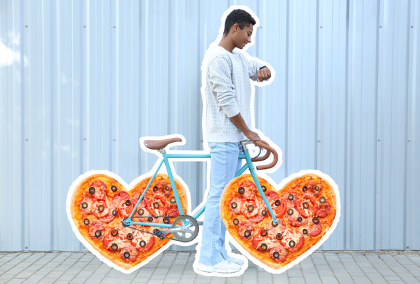African-American teenage boy and bicycle with heart shaped pizza instead of wheels outdoors - 写真・画像