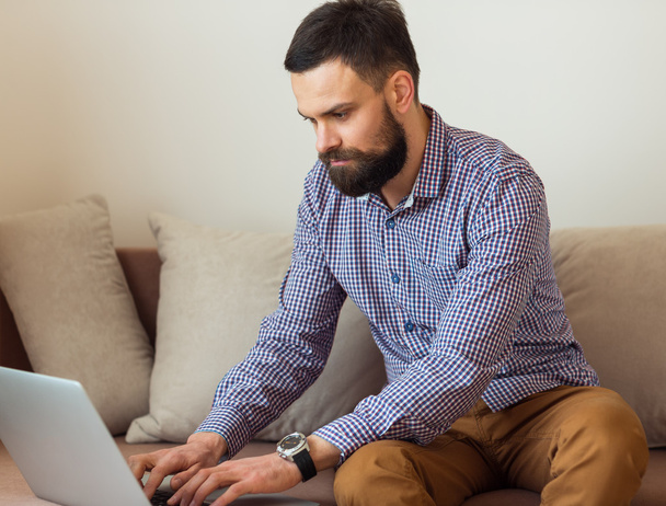 Fiatal szakállas ember dolgozik a laptop otthon - Fotó, kép