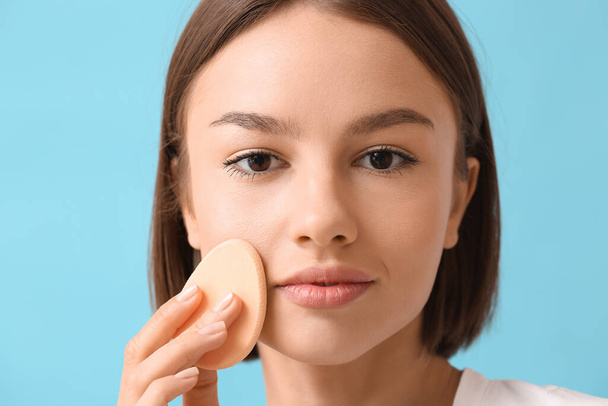 Pretty young woman with makeup sponge on blue background, closeup - Foto, immagini