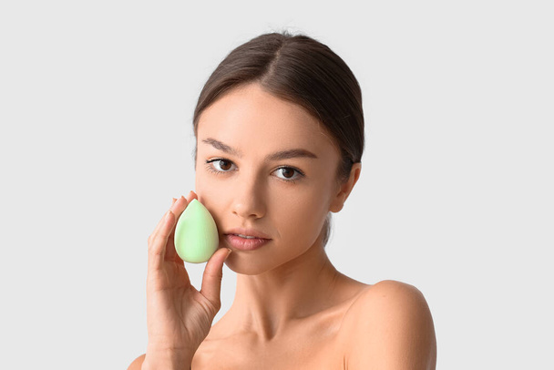Pretty young woman with green makeup sponge on grey background, closeup - Photo, Image