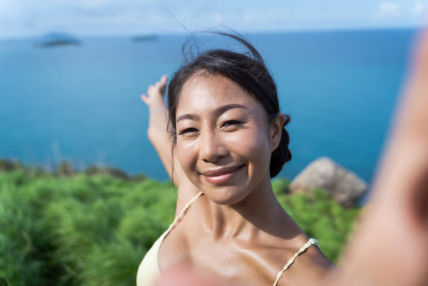 Young Asian woman taking a selfie photo with her mobile phone while traveling in the mountain trail with beach sea view - Фото, зображення
