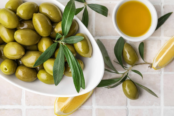 Bowls of green olives, oil and lemon slices on color tile, closeup - Foto, afbeelding