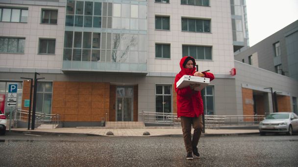 A delivery man in red clothes crossing the street. Mid shot - Foto, imagen