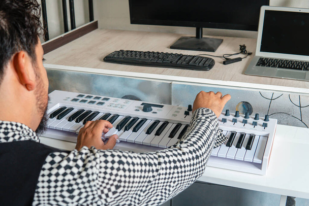 Музичний продюсер складає пісню з клавіатурою і комп'ютером. Музикант з рокерським стилем, одягнений в картату сорочку і чорний жилет. Прикутий музикант біля клавіатури. Іспанський композитор - Фото, зображення