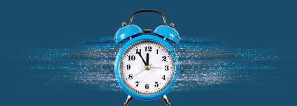 Abstract image of an alarm clock from which particles come off forming a stream. Dispersion on blue background - 写真・画像