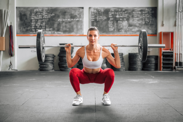 Ajuster haltérophilie féminine dans les leggings et soutien-gorge faire haltère dos squat pendant l'entraînement fonctionnel dans la salle de gym spacieuse en journée - Photo, image