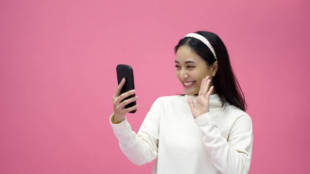 Jovem mulher asiática usar telefone inteligente um para chamada de vídeo em um fundo de estúdio rosa - Foto, Imagem