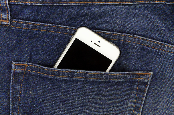 Parte do celular branco móvel no bolso traseiro da ganga azul
  - Foto, Imagem