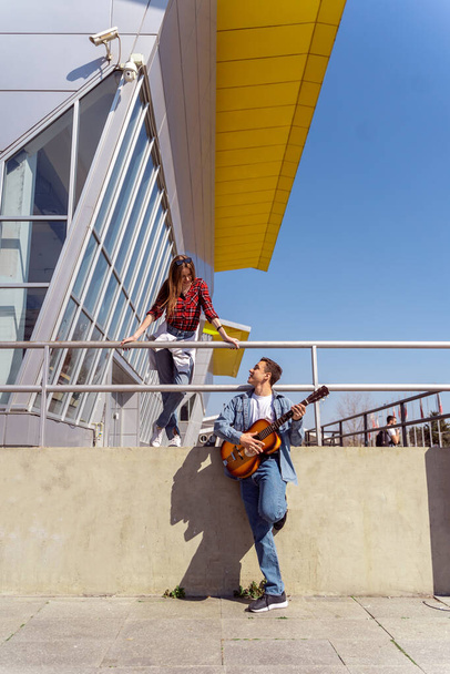 Милая пара, стоящая у забора, пока мальчик играет на гитаре - Фото, изображение