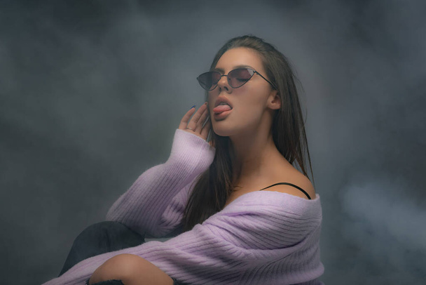 Atractiva y hermosa chica está posando y sosteniendo su postura mientras tiene vapor a su alrededor - Foto, Imagen