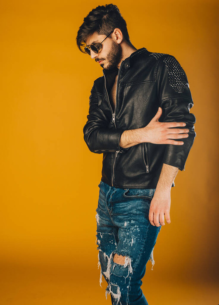 Attractive man posing in ripped blue jeans and fancy leather jacket - Фото, изображение