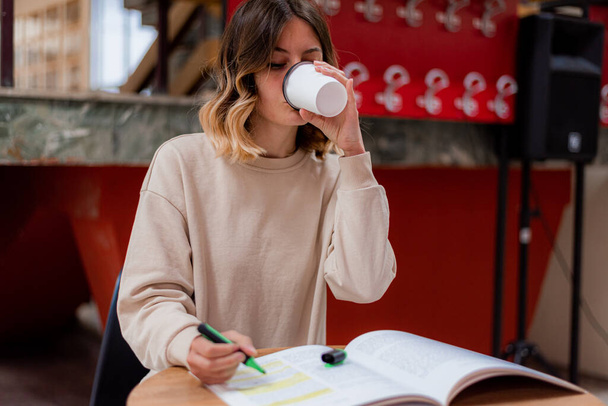 College ragazza bere caffè mentre lei sta leggendo per il college nella sala studio - Foto, immagini