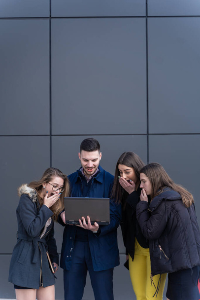 Группа молодых бизнесменов смотрит на ноутбук и смеется. - Фото, изображение