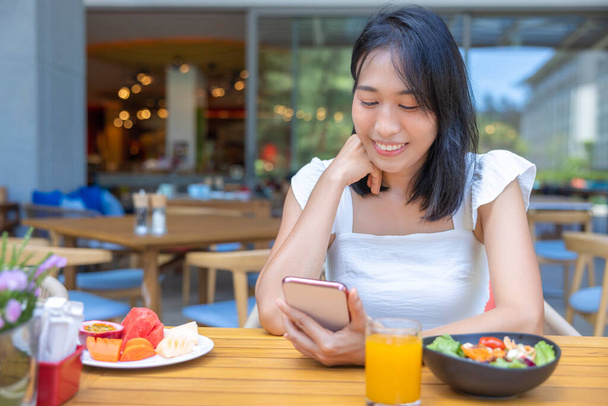 Woman eating Breakfast and play smart phone. Fruits such as watermelon, papaya, melon, passion fruit, orange juice and coffee. placed on a gray placemat. - Foto, afbeelding