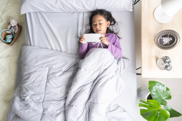 Top view Asian child little girl playing smartphone lying on the bed - Photo, image