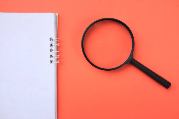 top view a Magnifying glass  with notebook isolate on a orange background. Searching concept. - Photo, Image