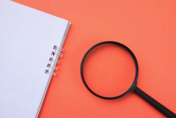top view a Magnifying glass  with notebook isolate on a orange background. Searching concept. - Foto, Imagen