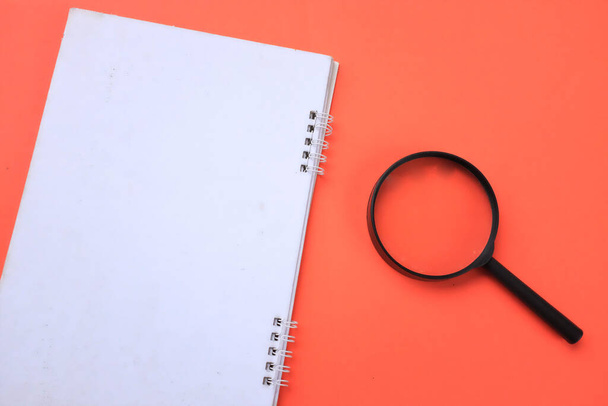 Magnifying glass  with notebook isolate on a orange background. Searching concept. - Foto, Imagen