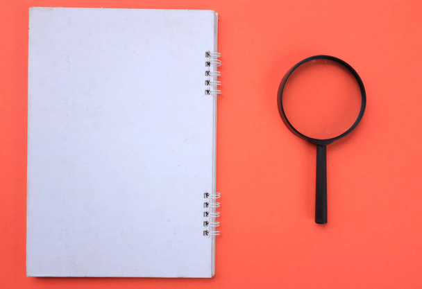 Magnifying glass  with notebook isolate on a orange background. Searching concept. - Fotografie, Obrázek