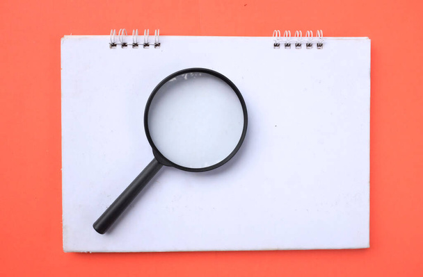 Magnifying glass  with notebook isolate on a orange background. Searching concept. - Foto, Imagen
