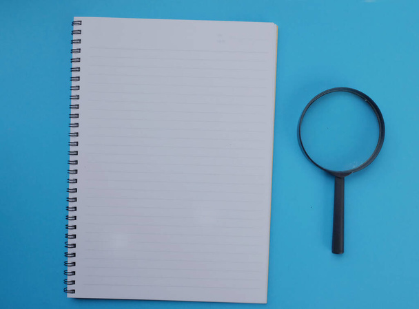 Lupe mit Notizbuch isoliert auf blauem Hintergrund. Suchkonzept. - Foto, Bild