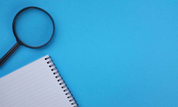 Magnifying glass  with notebook isolate on a blue background. Searching concept. - Foto, imagen