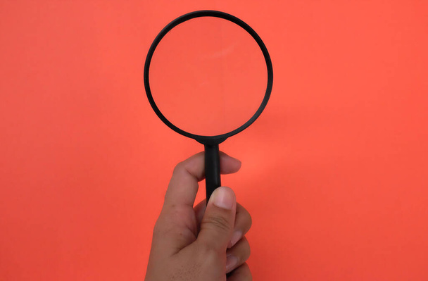 man hand holding magnifying glass isolate on a orange background.Searching concept. - Photo, Image