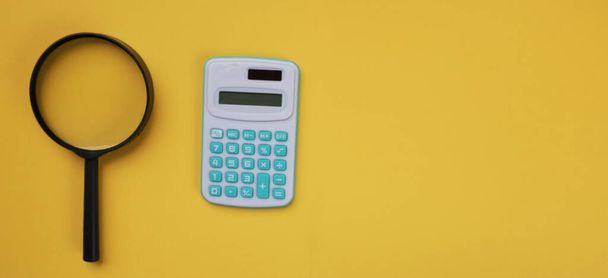 copy space a calculator and a black magnifying glass are on a yellow background. - Foto, Imagem