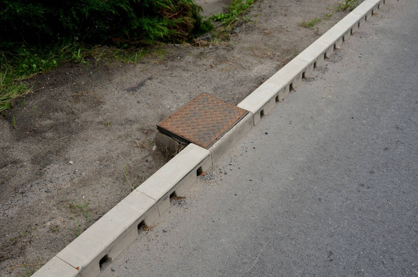 drainage hidden on the edge of an asphalt road Drainage system hidden in a perforated concrete gray curb. the water along the entire length of the road drains into the sewer through holes - 写真・画像