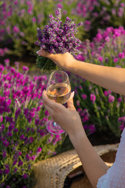 The girl is resting in a lavender field, drinking wine. Selective focus. Relaxation - Zdjęcie, obraz